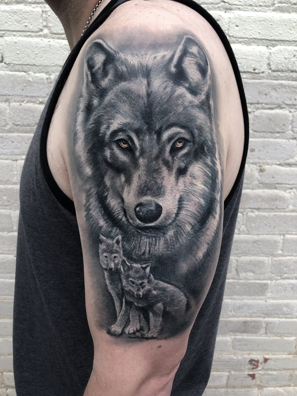Realistic black and grey wolf and pups tattoo on upper arm.