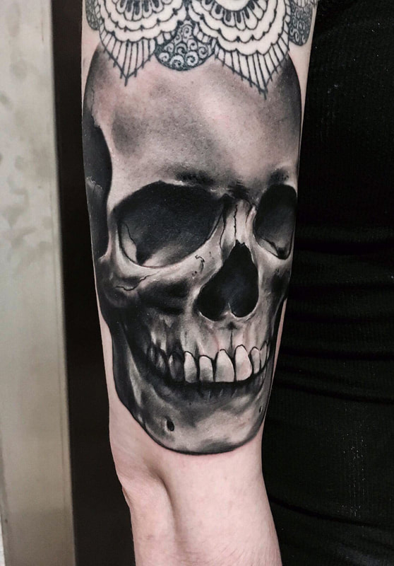 Realistic black and grey skull tattoo on an arm.