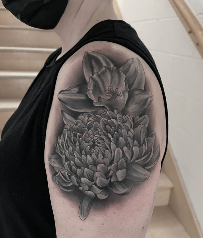 Realistic black and gray daffodil and chrysanthemum tattoo on a shoulder.