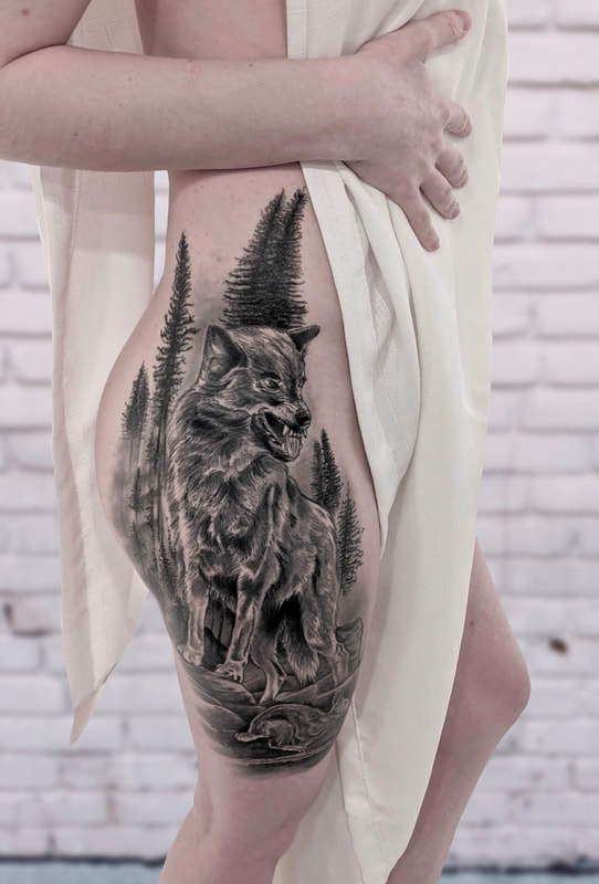 Realistic black and grey tattoo with a wolf, rabbit, and trees on an upper leg.