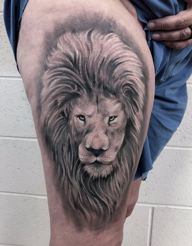 Black and grey realistic lion face tattoo on a thigh.