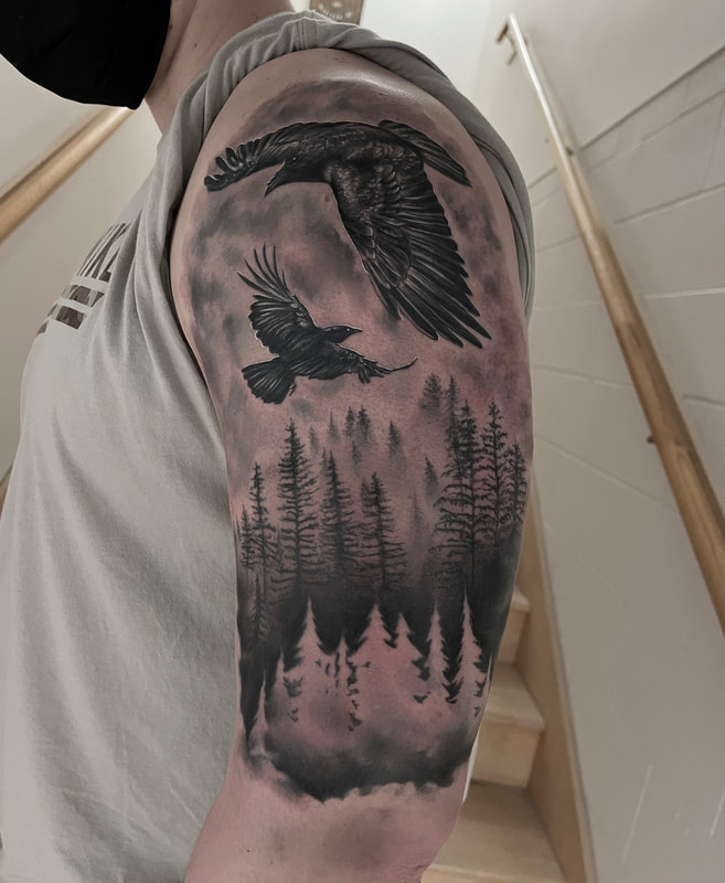 Black and grey realistic tattoo of crows flying above a forest scene on an upper arm.