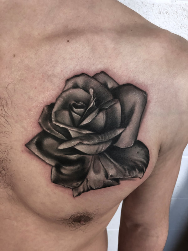 Black and gray realistic rose tattoo on a man's chest.